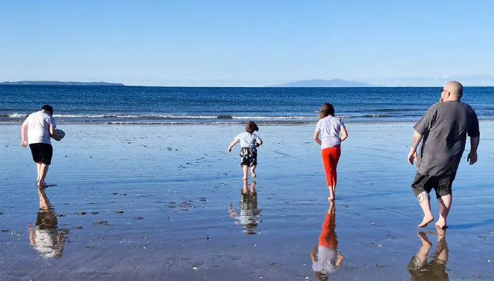 image at a beach, three children and one adult are walking towards the sea. it is sunny and wintry