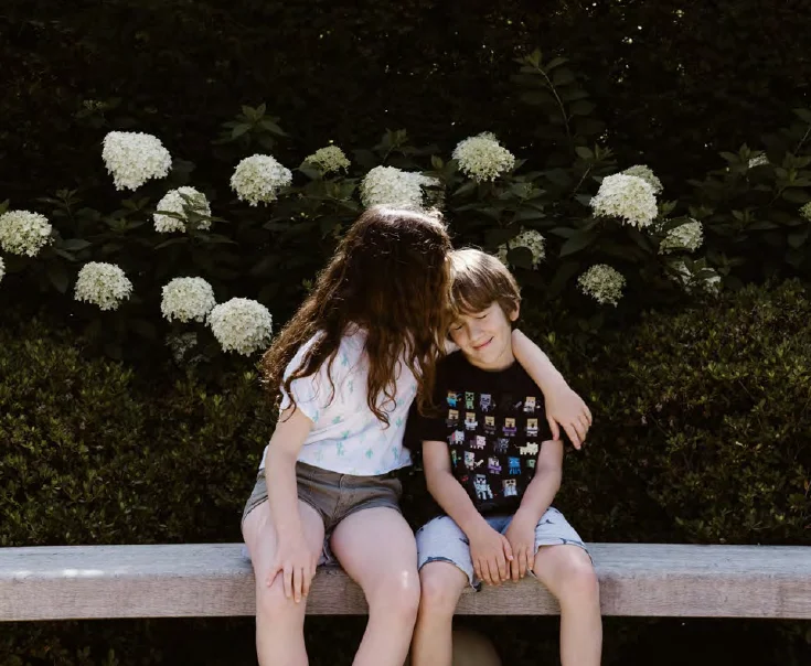 siblings hug while sitting on a wall