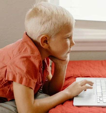 a young boy sitting on a bed using a laptop
