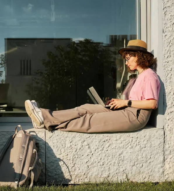 a student sitting on a ledge and using their laptop