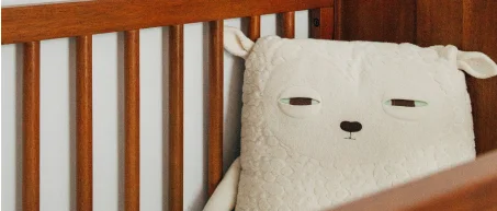 a tired looking large teddy bear in a cot