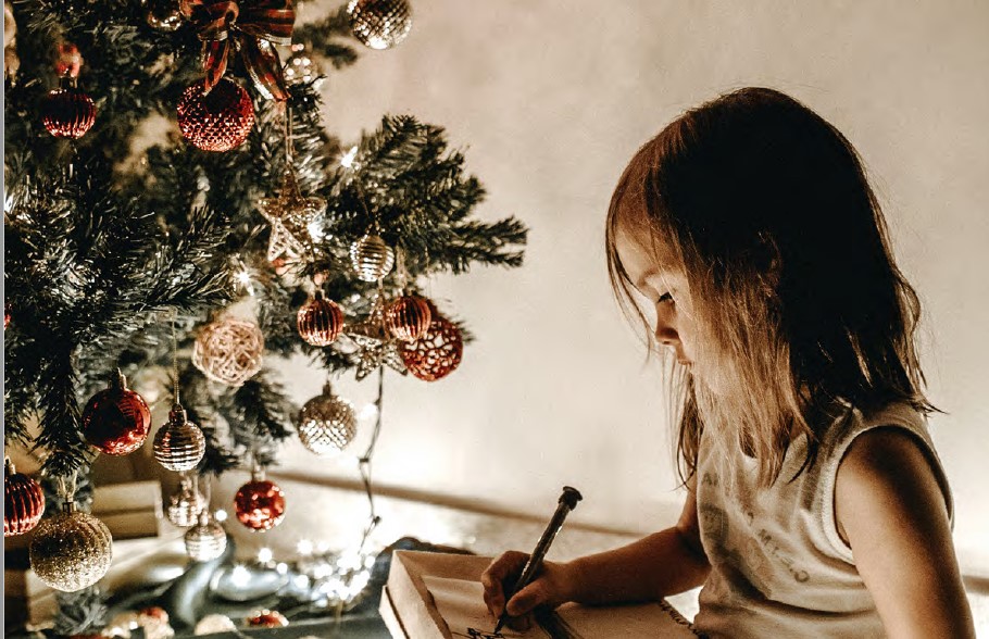 a child sits in front of a christmas tree. they are engrossed in playing with a gift